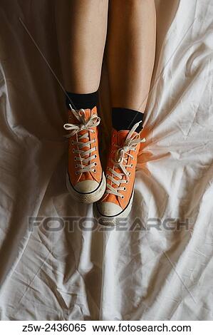 Stock Photography - Close up, young girl wearing sneakers and she lying on the bed, white sheets.. Fotosearch