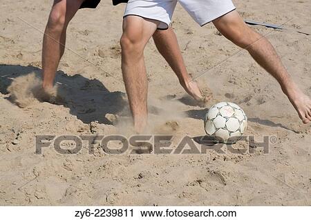 Stock Image - Closeup of legs, sand and soccer ball in action. Ahus Beach Soccer tournament 2014.. Fotosearch