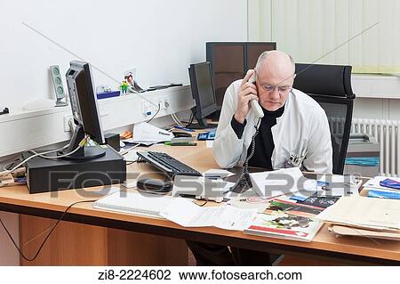 Stock Image - Doctor at his desc talking on the telephone.. Fotosearch