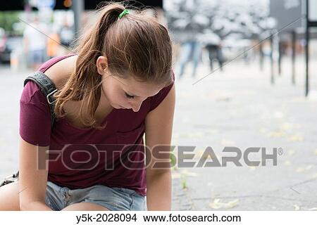 Picture - Hardenbergstrasse, West-Berlin, Berlin, Germany. Young, brunette woman, looking down, while sitting on the pavement of of a street, while reading a map.. Fotosearch