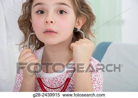 Little girl sitting on a medical couch and listening to her heart with a stethoscope View Large Photo Image Stock Photography - Little girl sitting on a medical couch and listening to her heart with a stethoscope. Fotosearch