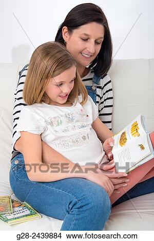 Little girl sitting on her mother's lap, and reading a book in her bedroom View Large Photo Image Picture - Little girl sitting on her mother's lap, and reading a book in her bedroom. Fotosearch