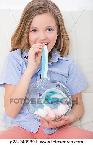 Little smiling girl eating white and blue marshmallow and holding a glass jar full of sweets View Large Photo Image Stock Image - Little smiling girl eating white and blue marshmallow and holding a glass jar full of sweets. Fotosearch
