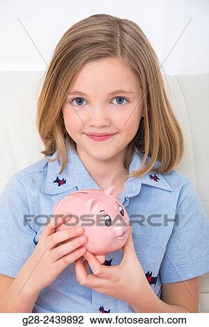 Stock Image - Little smiling girl holding a piggy bank. Fotosearch