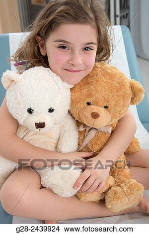 Little smiling girl holding two teddy bears in a paediatrician surgery View Large Photo Image Picture - Little smiling girl holding two teddy bears in a paediatrician surgery. Fotosearch