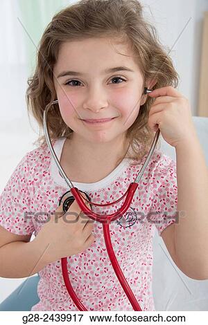 Little smiling girl sitting on a medical couch and listening to her heart with a stethoscope View Large Photo Image Stock Photo - Little smiling girl sitting on a medical couch and listening to her heart with a stethoscope. Fotosearch