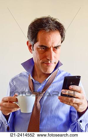 Stock Image - Man preparing to go to work. Holding a cup of coffee and checking the mobile phone.. Fotosearch