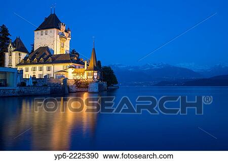 Stock Image - Oberhofen Castle at Lake Thun with mountains at night, Oberhofen, Switzerland.. Fotosearch