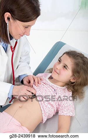 Stock Photo - Paediatrcian doctor examining little girl lying on medical couch, with her stethoscope. Fotosearch