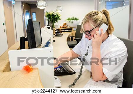 Tilburg, Nederland. Young, blonde nurse, doing her work as a receptionist at the main desk of the orthopedics nursing ward. View Large Photo Image Stock Photo - Tilburg, Nederland. Young, blonde nurse, doing her work as a receptionist at the main desk of the orthopedics nursing ward.. Fotosearch