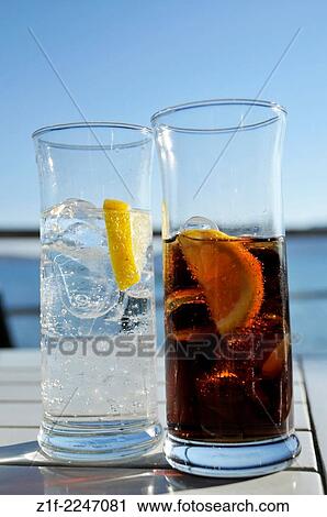 Stock Image - Two glasses filled respectively with a dark and transparent liquid.. Fotosearch