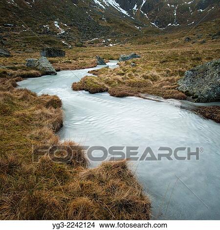 Water flows through a melting mountain stream of ice, Flakstadøy, Lofoten Islands, Norway. View Large Photo Image Picture - Water flows through a melting mountain stream of ice, Flakstadøy, Lofoten Islands, Norway.. Fotosearch