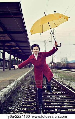 Woman balancing on one leg standing on railway track holding umbrella. View Large Photo Image Stock Image - Woman balancing on one leg standing on railway track holding umbrella.. Fotosearch