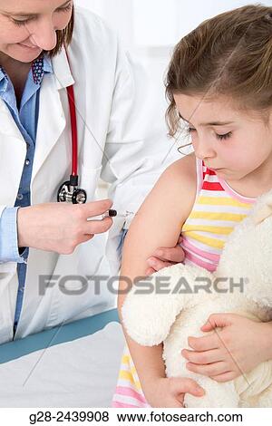 Woman doctor vaccinating a little girl holding her teddy bear View Large Photo Image Stock Photo - Woman doctor vaccinating a little girl holding her teddy bear. Fotosearch