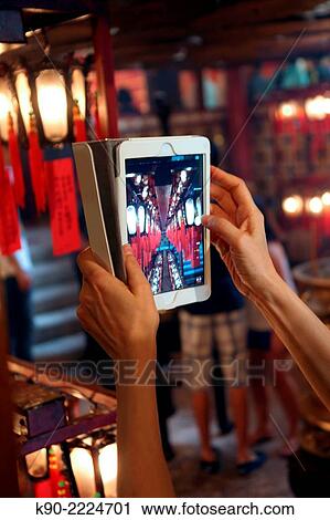 Stock Image - Woman holding her smartphone to take a picture from Man Mo temple in Sheung Wan, Hong Kong, China, East Asia.. Fotosearch