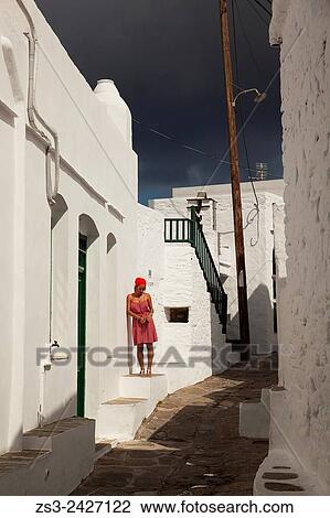 Stock Image - Woman posing in front of a whitewashed house in Faros village, Sifnos, Cyclades Islands, Greek Islands, Greece, Europe.. Fotosearch