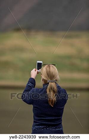 Stock Photo - Woman takiing a picture of the landscape with a smart phone, Hvalsnes in the Loni valley, Iceland.. Fotosearch