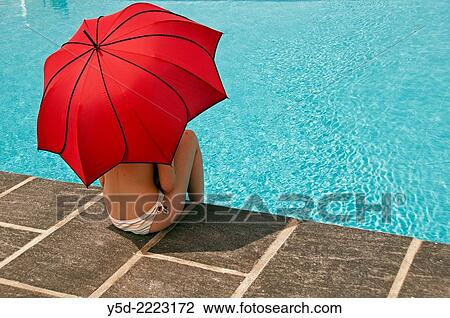 Stock Image - Woman with red umbrella, swimming pool. Fotosearch
