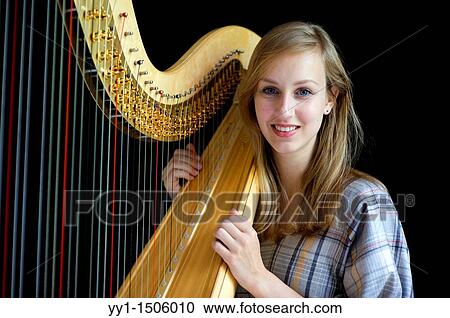Stock Image - Young, female student at conservatoire playing harp at graduate level.. Fotosearch