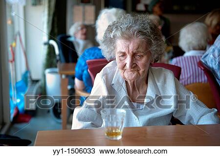 Stock Image - An elderly inhabitant of a Rotterdam nursing home with a glass of juice on the communal table.. Fotosearch