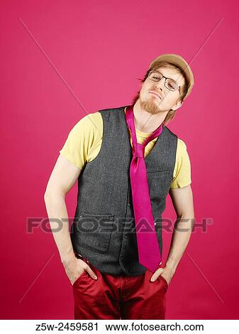 Stock Image - Expressive hipster wearing a vest and pink tie, pink background and studio shot.. Fotosearch