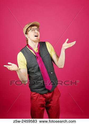 Stock Image - Expressive hipster wearing a vest and pink tie, pink background and studio shot.. Fotosearch