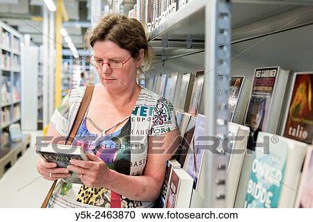 Gouda, Netherlands. Middle aged woman choosing a book to read from the library shelves. View Large Photo Image Stock Image - Gouda, Netherlands. Middle aged woman choosing a book to read from the library shelves.. Fotosearch