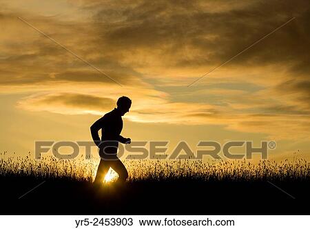 Stock Image - Man running in wildflower meadow at sunrise. Billingham, north east England, United Kingdom.. Fotosearch