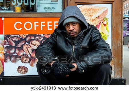 Stock Image - New York, USA. Homeless man of African American ethnicity, living in the streets of Manhattan, in front of a coffee shop.. Fotosearch