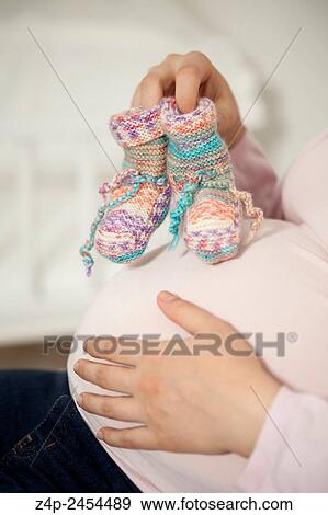 Stock Photo - Pregnant woman with baby shoes. Fotosearch