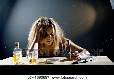 Stock Photo - Rotterdam, Netherlands. Depressed young woman playing with a knife and drinking a glass of wiskey.. Fotosearch