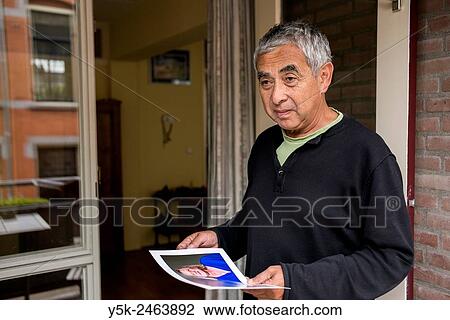 Tilburg, Netherlands. Middle aged Indonesian male holding a photo print, while standing near the balcony door of his apartment. View Large Photo Image Stock Image - Tilburg, Netherlands. Middle aged Indonesian male holding a photo print, while standing near the balcony door of his apartment.. Fotosearch