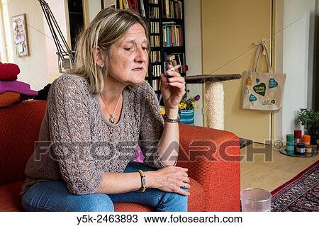 Tilburg, Netherlands. Middle aged woman, smoking a cigarette, while sitting on her living room coach. View Large Photo Image Stock Image - Tilburg, Netherlands. Middle aged woman, smoking a cigarette, while sitting on her living room coach.. Fotosearch