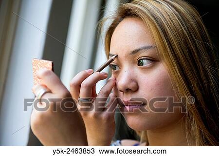 Stock Image - Tilburg, Netherlands. Studio portrait of a young Chinese girl doing her make up.. Fotosearch