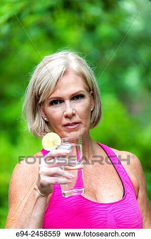 56 year old blond woman holding a glass of water to her head to cool off. View Large Photo Image Stock Photo - 56 year old blond woman holding a glass of water to her head to cool off.. Fotosearch