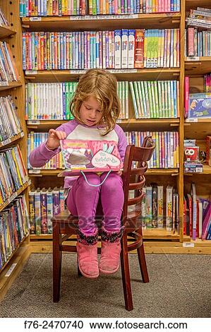 Stock Image - 6 year old girl in pink outfit, reading in the childrens' section of an upscale bookstore in Berkeley, CA. MR# 6063.. Fotosearch