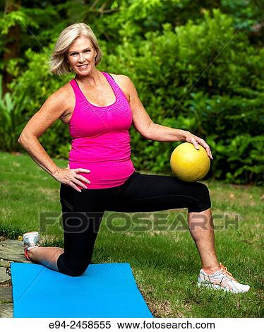 Stock Photography - A 56 year old blond woman in fitness clothing on one knee in a back yard.. Fotosearch