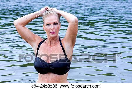 A 56 year old blond woman looking at the camera in in a bikini top standing in front of water. View Large Photo Image Stock Photograph - A 56 year old blond woman looking at the camera in in a bikini top standing in front of water.. Fotosearch