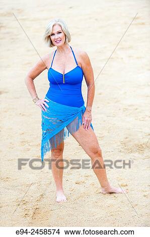 A 56 year old blond woman wearing a swim suit standing on a beach. View Large Photo Image Picture - A 56 year old blond woman wearing a swim suit standing on a beach.. Fotosearch