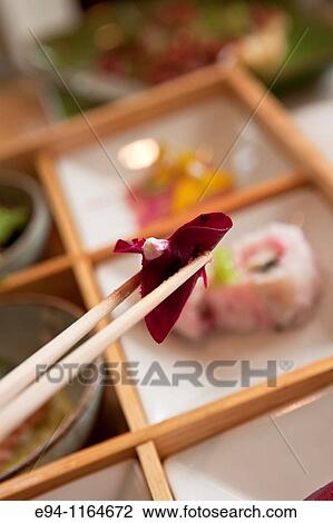 A piece of sushi being held in chopsticks over a plate of sushi in a restaurant. View Large Photo Image Stock Image - A piece of sushi being held in chopsticks over a plate of sushi in a restaurant.. Fotosearch