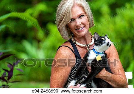 A portrait of a 56 year old blond woman smiling directly at the camera and holding a cat, outdoors.. View Large Photo Image Stock Image - A portrait of a 56 year old blond woman smiling directly at the camera and holding a cat, outdoors... Fotosearch