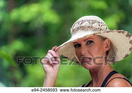 A portrait of a 56 year old blond woman wearing a straw hat and looking directly at the camera, outdoors. View Large Photo Image Stock Image - A portrait of a 56 year old blond woman wearing a straw hat and looking directly at the camera, outdoors.. Fotosearch