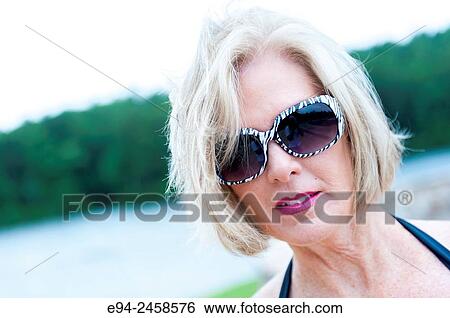 A portrait of a 56 year old blond woman wearing sunglasses looking directly at the camera, outdoors. View Large Photo Image Stock Photograph - A portrait of a 56 year old blond woman wearing sunglasses looking directly at the camera, outdoors.. Fotosearch