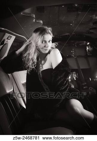 Stock Image - Attractive blond girl posing inside the limousine, tinted black and white image.. Fotosearch