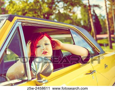 Stock Image - Beautiful young woman posing, old Dodge - 70's theme, intentional film grain added.. Fotosearch