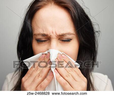Stock Photo - Close up, young woman blowing her nose, gray background.. Fotosearch