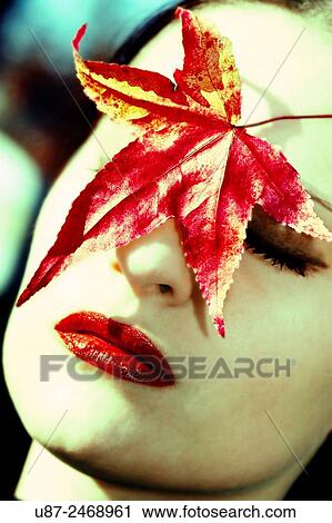 Stock Image - Closeup of Young Female headshot with colorful leaves next to her face... Fotosearch