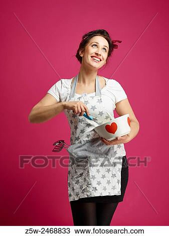 Stock Image - Funny housewife and kitchen utensils, pink background.. Fotosearch