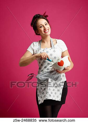 Stock Photography - Funny housewife and kitchen utensils, pink background.. Fotosearch