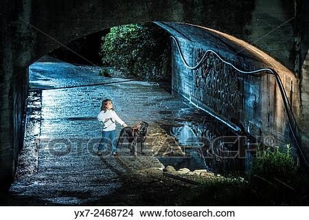 Picture - Lonely girl with her pet dog in a tunnel at night time.. Fotosearch